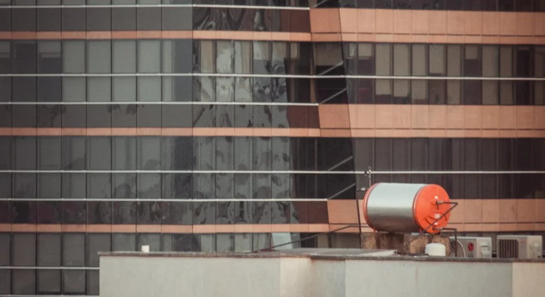 Orange and white rooftop water storage tank on top of a modern glass-fronted building