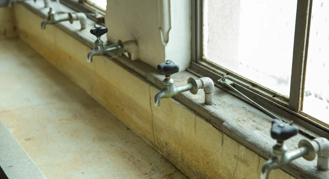 Row of wall-mounted outdoor faucets along a window ledge, illustrating plumbing valve hardware.