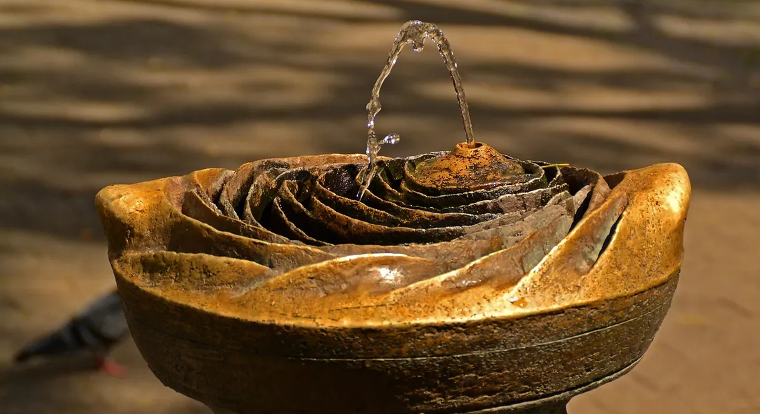 Close-up of a weathered, rust-covered circular metal container with a small stream of water flowing from a nozzle at the top.