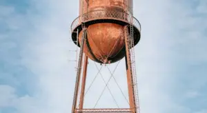 Rusty metal water storage tank elevated on a metal framework against a clear blue sky