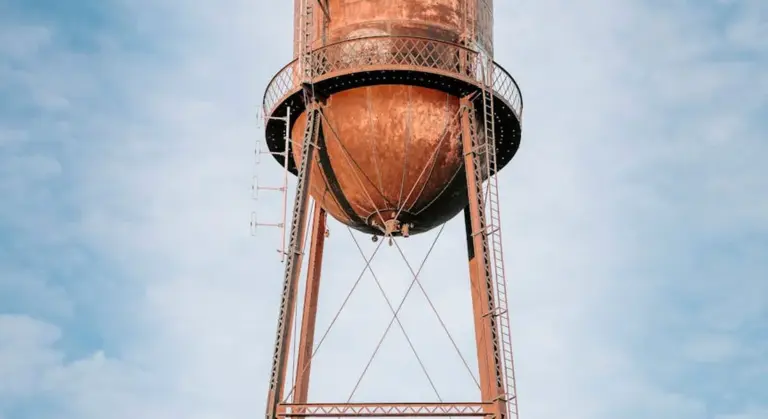Rusty metal water storage tank elevated on a metal framework against a clear blue sky