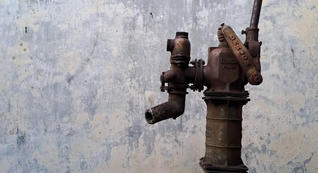 A rusted sump pump valve mounted on a textured, peeling blue-gray wall.