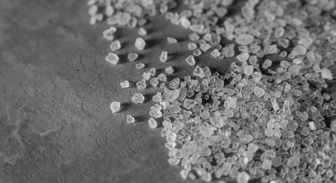 Close-up of small white salt pellets scattered on a dark surface