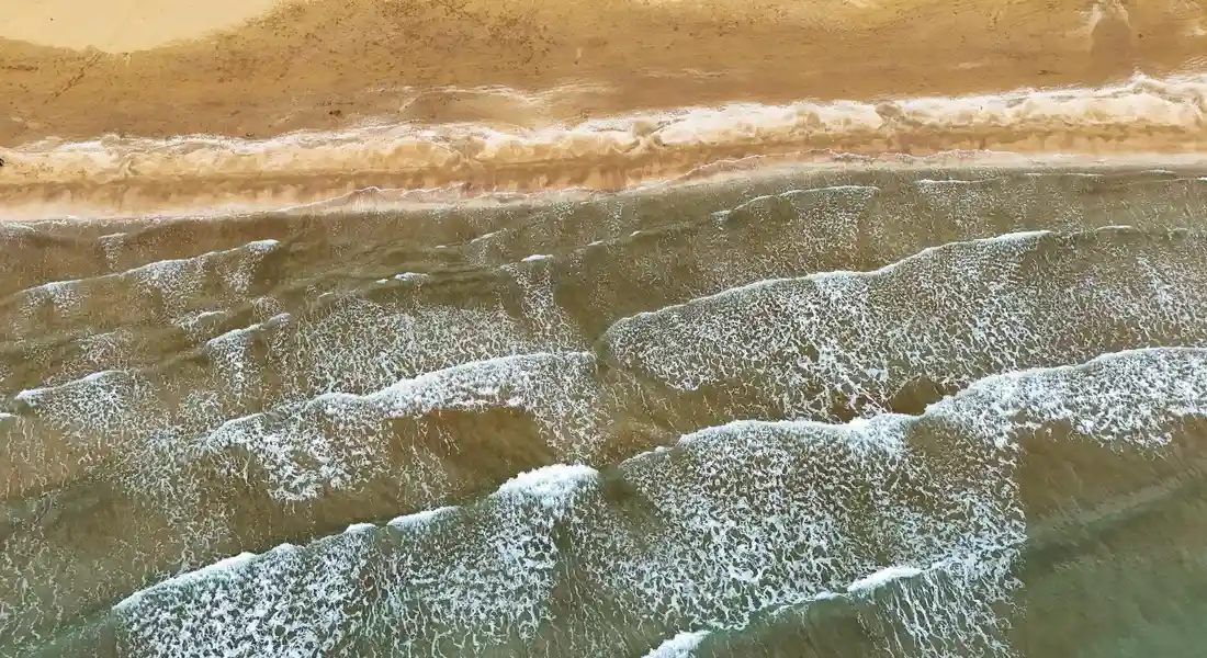 Foamy white waves cascading onto a sandy shoreline along the coast.