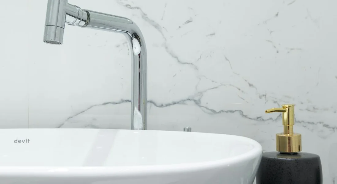 Close-up of a white sink with a chrome faucet and a black soap dispenser against a marble-patterned wall.