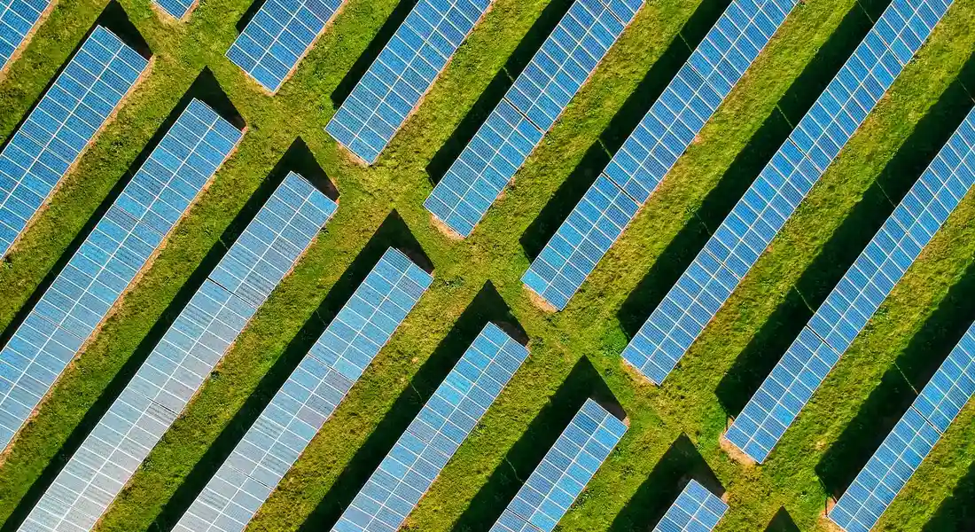 Aerial view of long rows of solar panels installed on a grassy field.