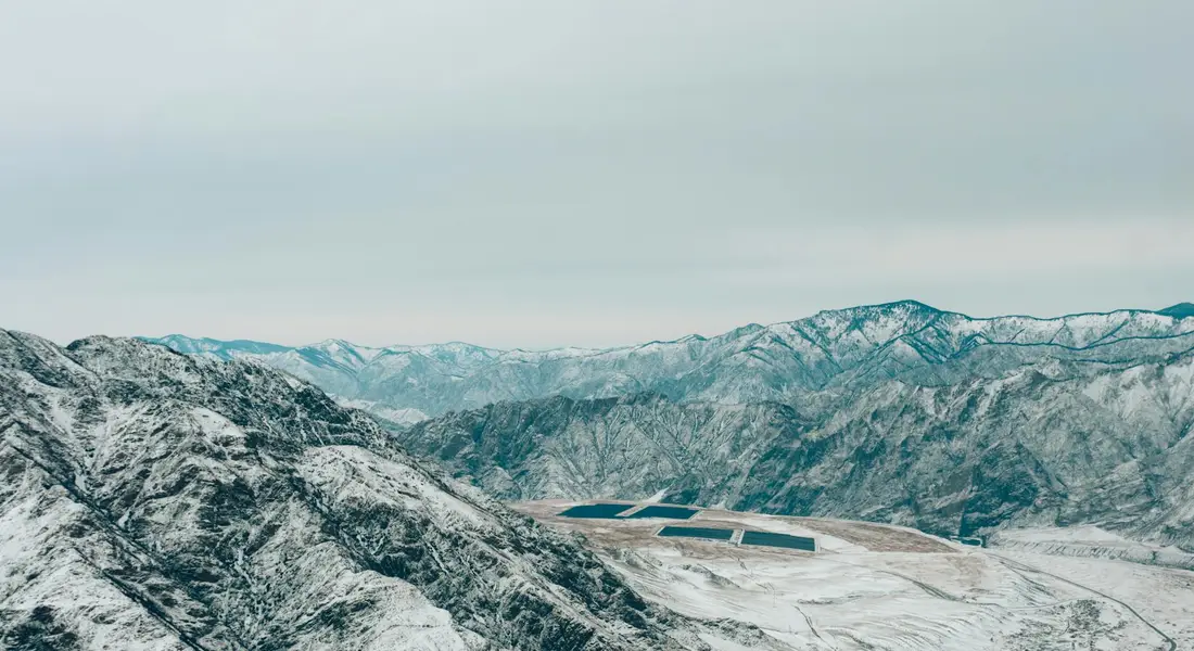 Snow-covered mountains with a solar thermal panel array installed on a hillside.