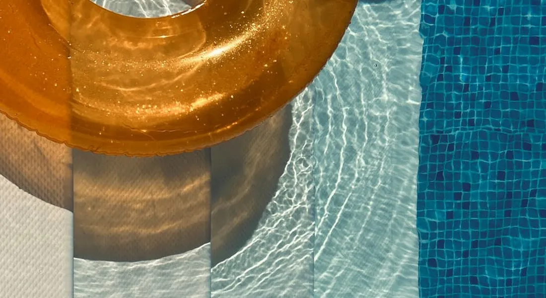 Close-up of a pool edge with orange circular object and blue mosaic tiles reflecting on the water
