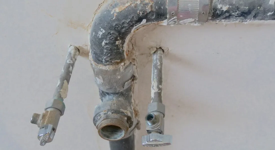 Close-up of corroded water supply fittings under a sink, with mineral buildup and a seized valve on copper piping.
