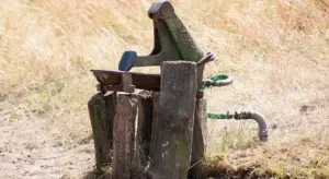 An old outdoor water pump with a handle and hose, situated in a dry grassy field