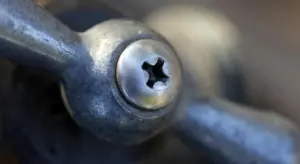 Close-up of a metal plumbing fitting with a Phillips-head screw showing a threaded joint.