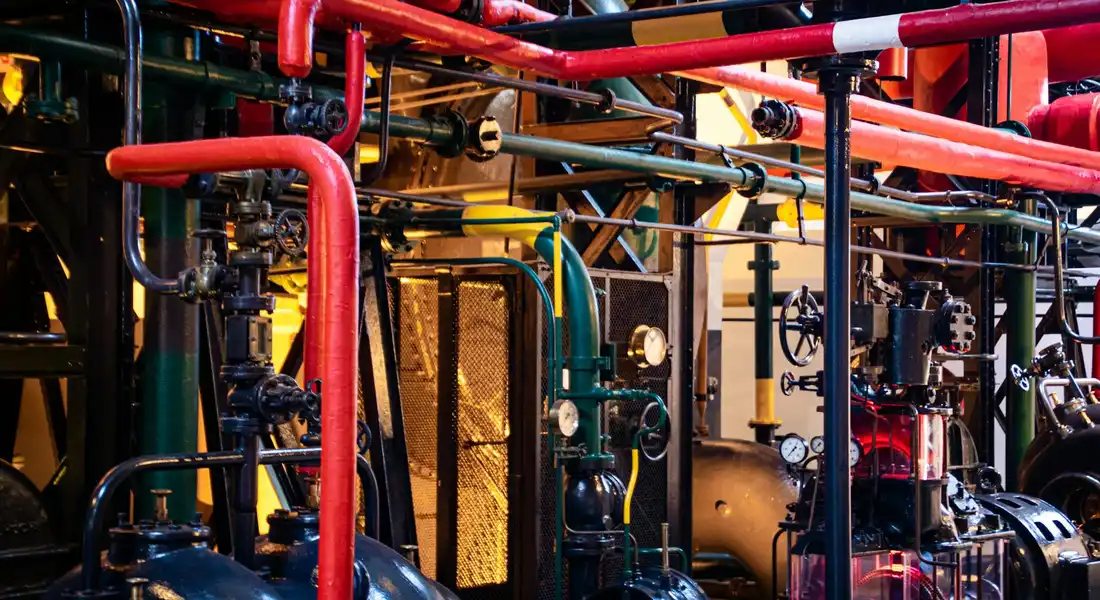 Industrial mechanical room with red and green pipes, valves, and gauges illustrating plumbing for sump pump drainage