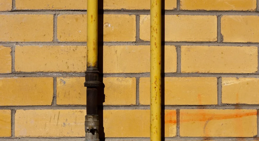 Two vertical yellow pipes mounted on a yellow brick wall, representing sump pump drainage lines.