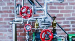 Close-up of red-handled valves and metal pipes mounted on a brick wall, forming part of a basement sump pump system.