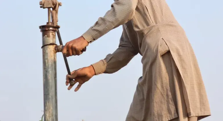 Close-up of a person operating a manual pump handle on a vertical metal pipe outdoors.