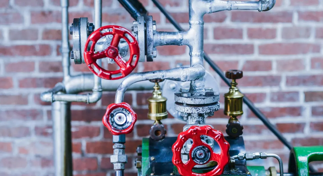 Close-up of sump pump piping with red valve handles and gauges against a brick wall