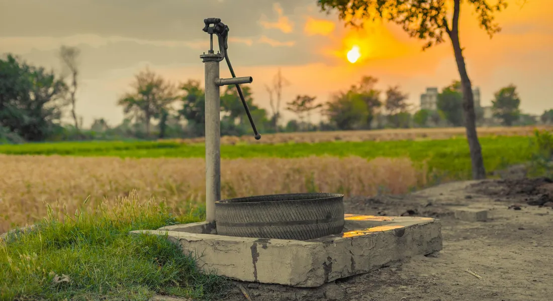 Old hand water pump on a concrete pedestal in a field at sunset, symbolizing planning and maintenance for water systems