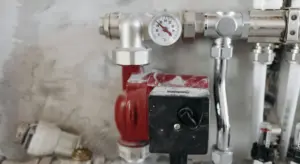 Close-up of a sump pump installation featuring a red motor housing, a pressure gauge, and connected metal piping