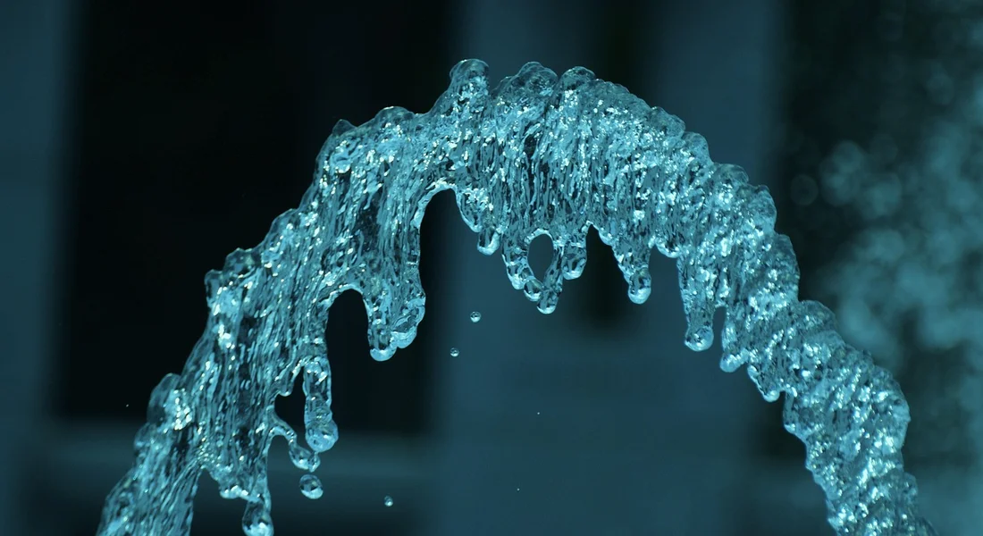 Blue-tinted arc of water spraying from a sump pump discharge against a dark background.