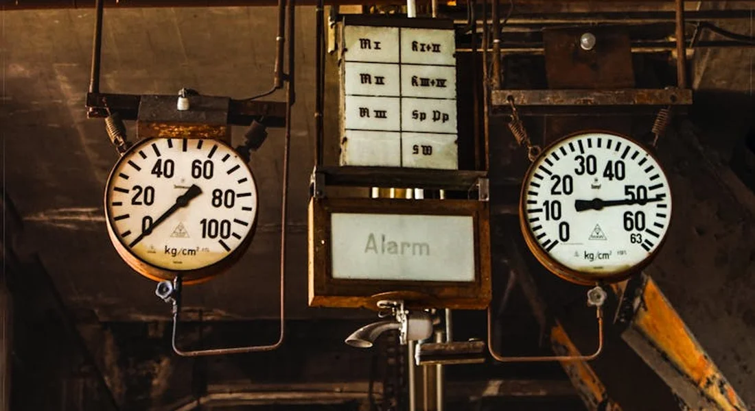 Two circular pressure gauges flank a central alarm display labeled 'Alarm' in an industrial basement mechanical room.