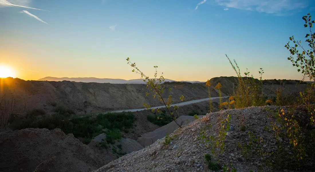 Sunset over an excavation site with dirt piles and a narrow trench illustrating sump pit prep.