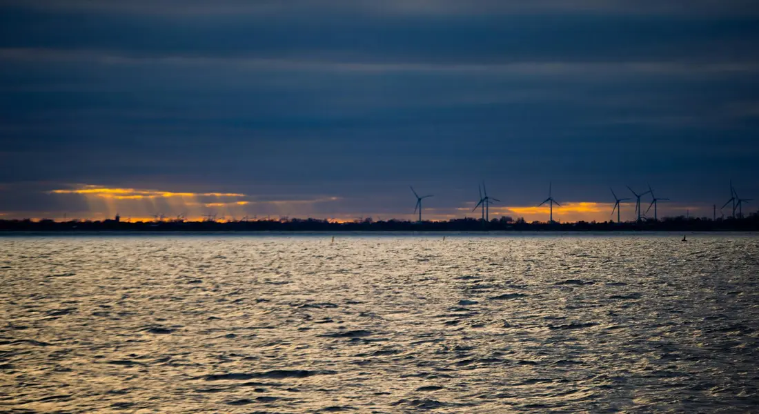 Sunset over a lake with wind turbines on the horizon.