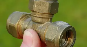 Close-up of a brass toilet water supply valve fitting being held by a person's finger.
