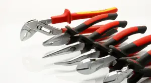 A row of pliers and other hand tools with red and black handles laid out on a white surface.