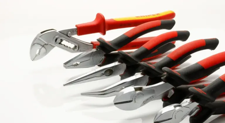 A row of pliers and other hand tools with red and black handles laid out on a white surface.