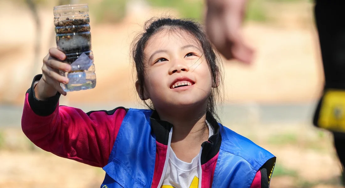 A young child outdoors holding a clear bottle of water, highlighting the importance of clean water