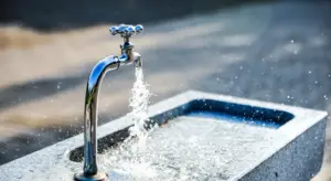 Close-up of a chrome faucet with running water over a compact stone sink, representing plumbing work for an under-sink filtration system.