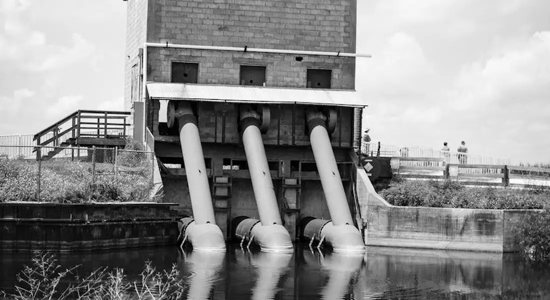 Industrial scene with three large pipes entering a waterway beneath a brick building