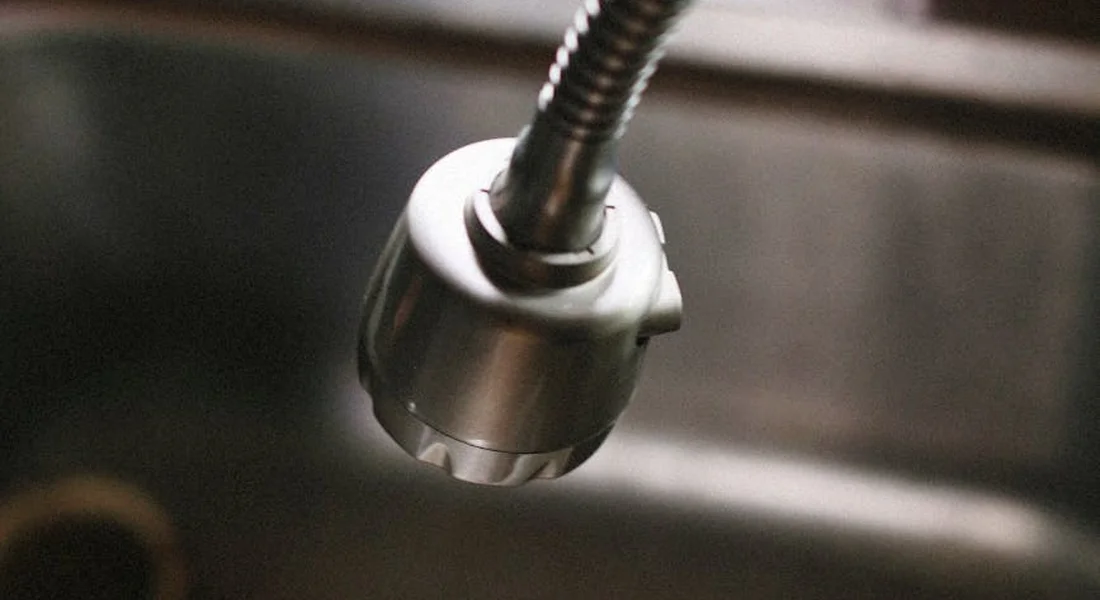Close-up of a metal shut-off valve with a flexible supply line under a kitchen or bathroom sink.