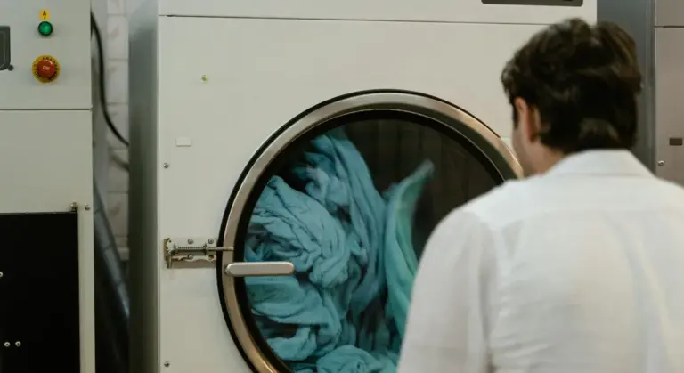 A technician in a white coat stands beside a front-loading washing machine with its door open, clothes visible inside, illustrating the washing process.