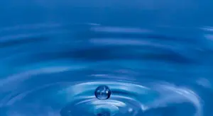 Close-up of blue water with ripples and a small droplet creating concentric waves.
