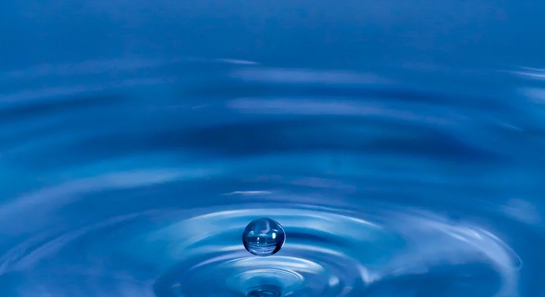 Close-up of a water droplet creating ripples on a blue water surface