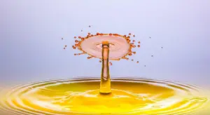 Close-up of a yellow water splash rising like a crown above a calm pool, with a pale blue background.