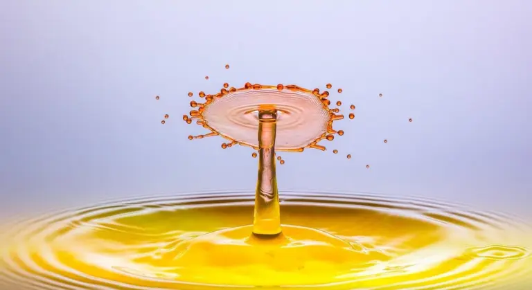 Close-up of a yellow water splash rising like a crown above a calm pool, with a pale blue background.