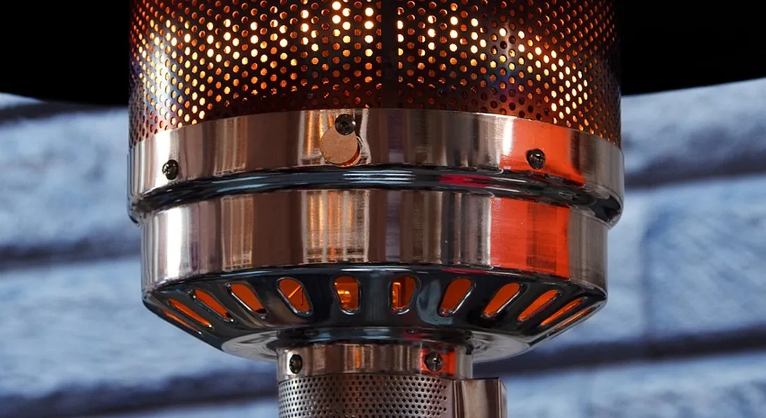 Close-up of a gas burner on a heating appliance, with metal mesh guard and ignition area.