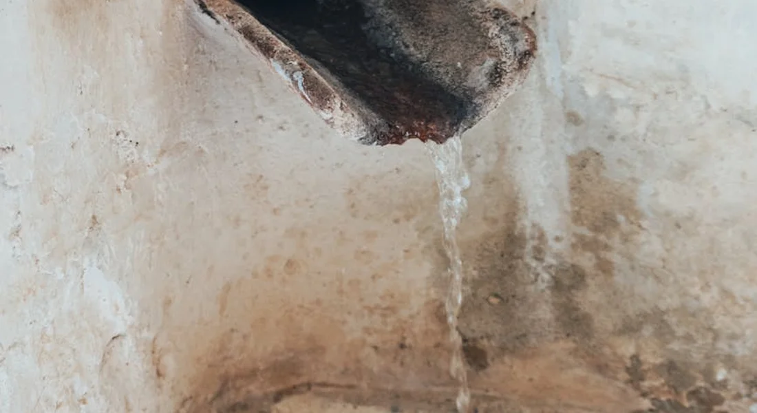 Close-up of a water leak dripping from a pipe onto a rough wall, illustrating the importance of proper line sizing.
