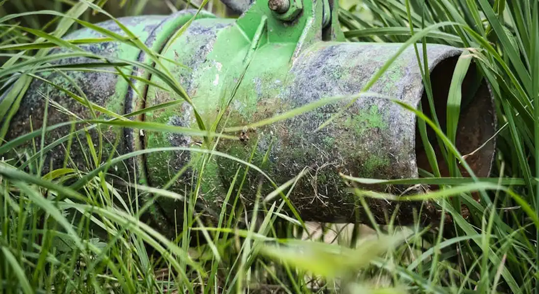Close-up of a green buried water main pipe partially obscured by tall grass