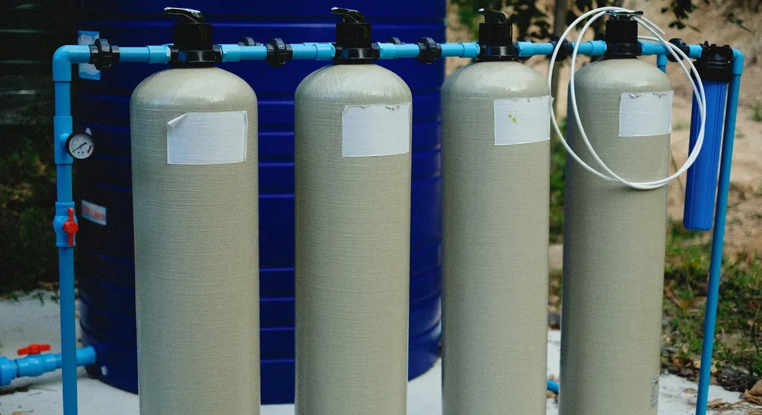 Three tall cylindrical water filtration tanks connected by blue tubing, set up outdoors for portable purification.