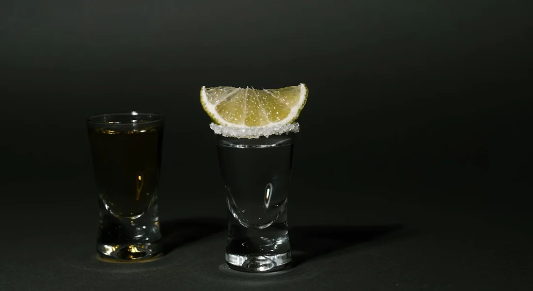 Two glasses on a dark surface; the tall glass has a salted rim and a lemon wedge, while a smaller glass sits beside it, illustrating a salt-related decision.