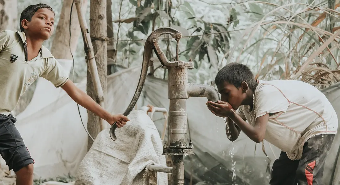 Two workers inspect a water source pump outdoors, examining pipes and fittings for a home heating and cooling system.