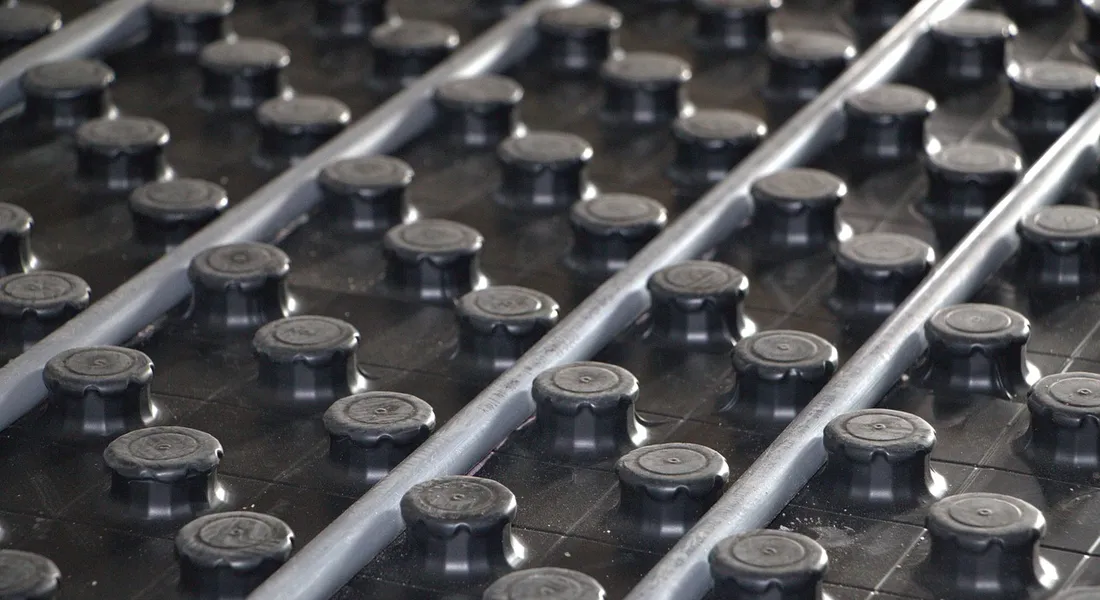 Close-up of a grid-like surface with many round black access caps and two diagonal metal pipes, representing buried loop components of a water source heat pump system.