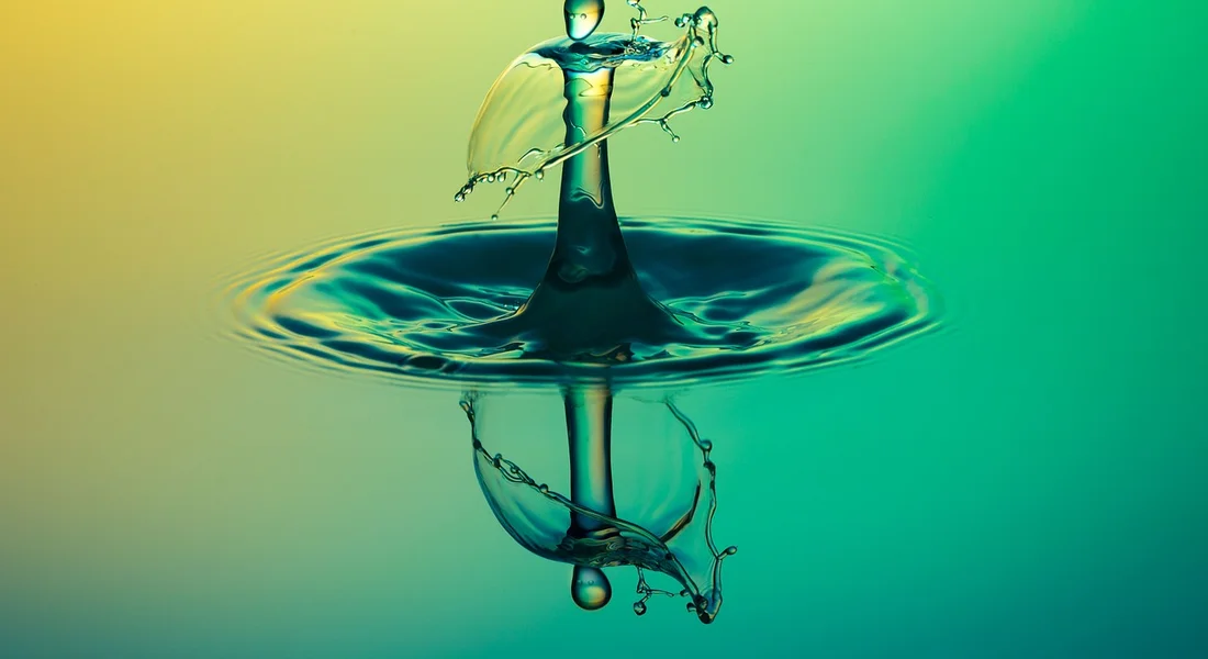 Close-up of a water droplet creating a splash on a calm surface with a vibrant gradient background in yellow and teal.