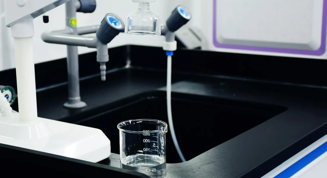 Close-up of a laboratory water filtration setup on a black countertop with tubing and a glass beaker in the foreground.