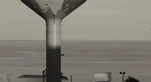 Exterior view of an elevated water storage tank mounted on a vertical pedestal with outlet piping visible against a cloudy sky.
