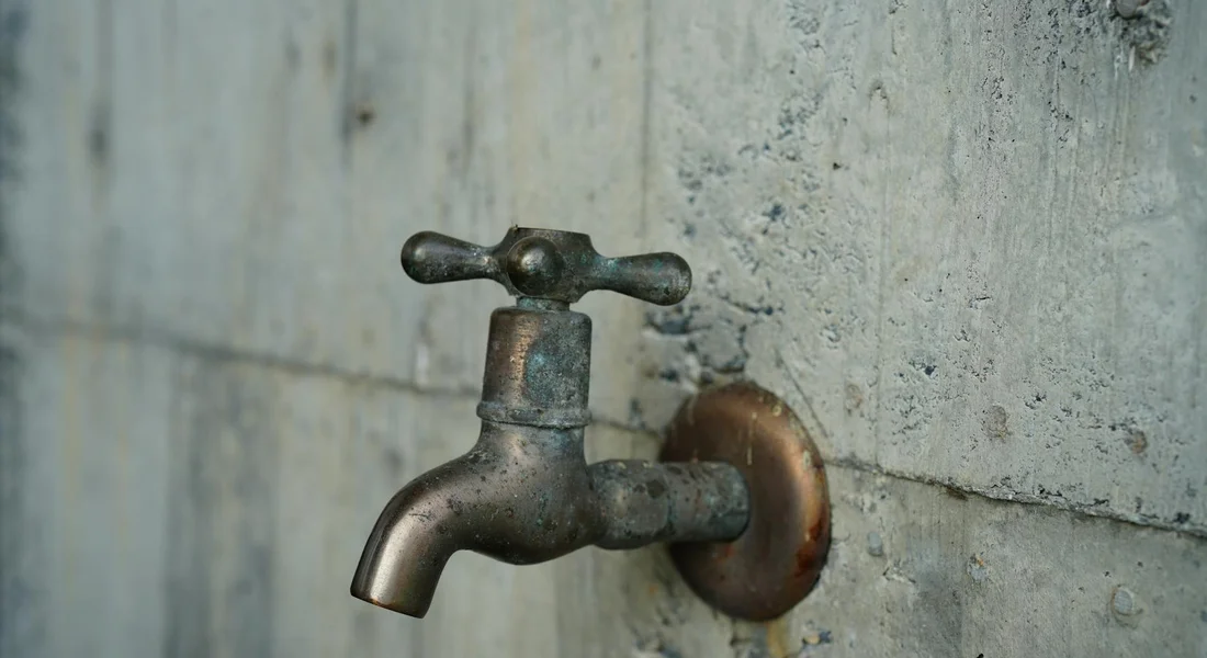 Metal outdoor water faucet mounted on a rough concrete wall with a curved spout