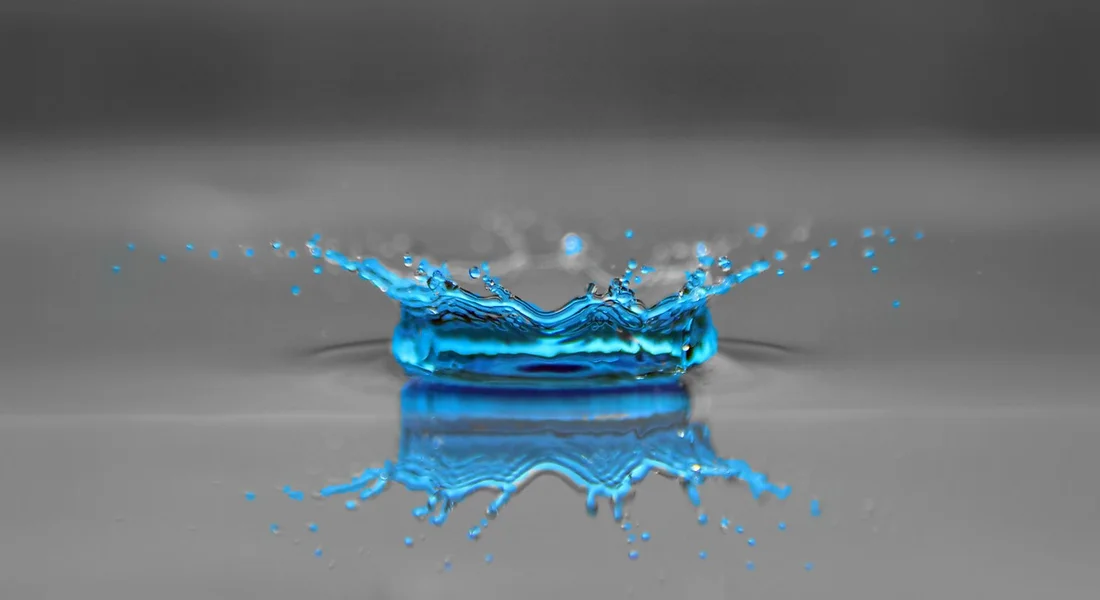 Blue water splash on a reflective gray surface, illustrating the concept of temperature and water in a heater.